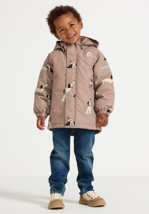 Gevoerde kinderjas in lichtbruin met hondenpatronen. Beschikt over een capuchon, elastische manchetten en reflecterende accenten. Draagt bij blauwe jeans en sneakers.