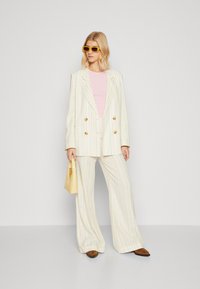Dubbelzijdige blazer van lichte gestreepte stof; brede broek in bijpassend ontwerp. Gekoeld met een roze top en een gele handtas.
