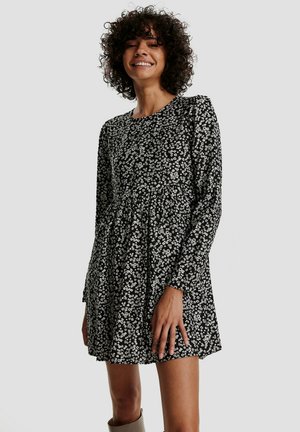Schwarzes Kleid mit langen Ärmeln, rundem Ausschnitt und floralem Muster in Weiß. Ausgestelltes Design mit gerafften Details an der Taille. Weiche Textur.