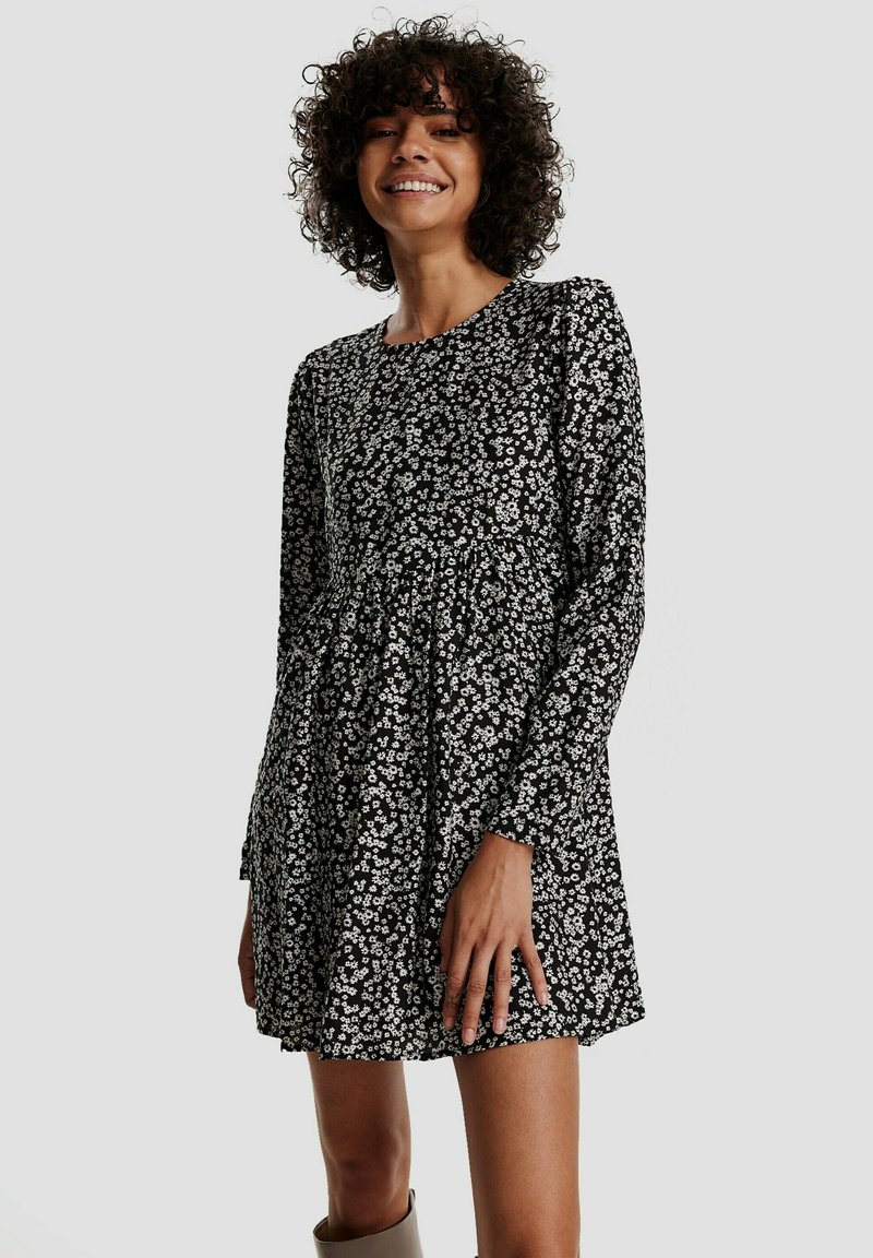 Schwarzes Kleid mit langen Ärmeln, rundem Ausschnitt und floralem Muster in Weiß. Ausgestelltes Design mit gerafften Details an der Taille. Weiche Textur.