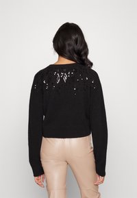 Czarny krótki sweter z długimi rękawami, wykonany z teksturowanej dzianiny, z dekoracyjnymi cekinowymi akcentami na plecach. Gładkie wykończenie z okrągłym dekoltem.