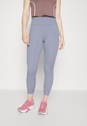 Leggings d'entraînement gris clair avec une taille haute, une texture lisse et un design ajusté, associés à des chaussures de sport roses.