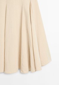 Beige, svajende nederdel med blødt stof og subtile folder ved den nederste kant mod en ensfarvet hvid baggrund.