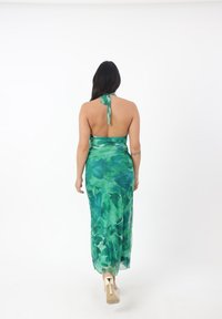 Abito maxi floreale verde con collo all'americana e schiena scoperta, caratterizzato da una texture simile alla seta e un design fluido. Accentuato da tacchi alti.