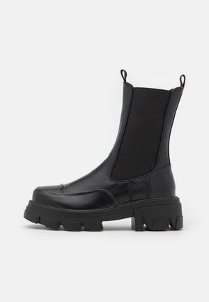 Botte noire à la cheville en cuir lisse, avec des panneaux latéraux élastiques, une semelle en caoutchouc épaisse et des tirettes intégrées pour un enfilage facile.