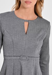 Graues Fischgrätkleid mit runder Ausschnitt und einem Schlüsselloch-Ausschnitt. Verfügt über lange Ärmel und eine taillierte Taille mit Gürtel.