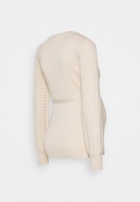 Pull en beige tricoté avec de longues manches à motifs et une taille cintrée. Dispose de poignets côtelés et d'un dos, d'une texture douce et sans fermetures visibles.
