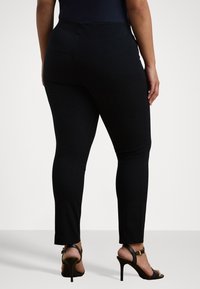 Leggings noirs avec une texture lisse, une taille haute et des jambes ajustées, associés à des sandales à talons ouverts.