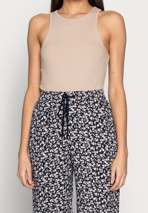 Beige, geripptes Tanktop kombiniert mit navyblauen, locker sitzenden Hosen mit Blumenmuster, die einen Kordelzugbund und weiße Blumenmuster aufweisen.