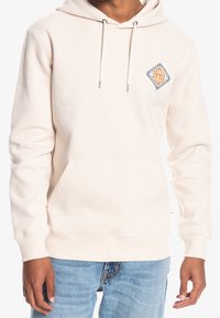 Krémová mikina s kapucí a přední kapsou, nastavitelné šňůrky a diamantová nášivka na levém prsu. Měkký materiál ze směsi bavlny.