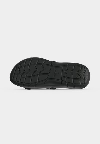 Semelle de chaussure noire avec un motif en zigzag et en grille, taille marquée au centre, sur fond blanc uni.