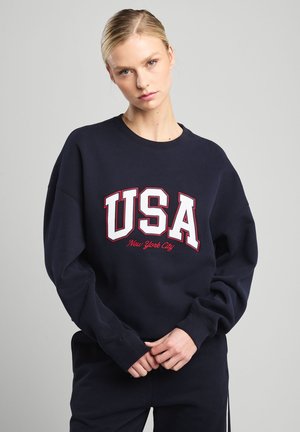Marine sweatshirt met lange mouwen, ronde hals en geborduurd "USA New York City" in wit en rood. Zacht materiaal en een relaxte pasvorm.