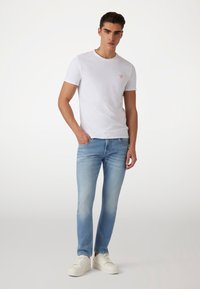 Camiseta blanca de manga corta con un pequeño logo rojo, combinada con jeans ajustados de color azul claro y zapatillas blancas. Tejido suave y diseño casual.