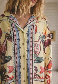 Cămașă cu nasturi din țesătură galbenă, decorată cu imprimeuri colorate cu tematică marină, guler cu model și accente decorative. Textură moale și croială lejeră.