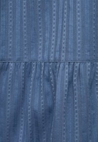 Textured blue fabric with vertical stripes and hexagonal patterns. The lower section features gathered fabric for added volume.