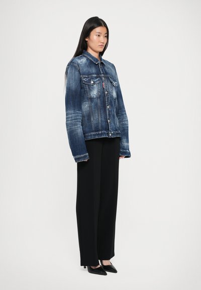 Denim jakna temno modre barve z zbledelostmi, prsni žepi in gumbi za zapiranje, v kombinaciji s črnimi širokimi hlačami in črnimi čevlji s konico.
