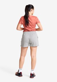 Idrottskläder med en åtsittande, rostfärgad kortärmad topp och grå shorts. Svarta och röda idrottsskor med vita strumpor.