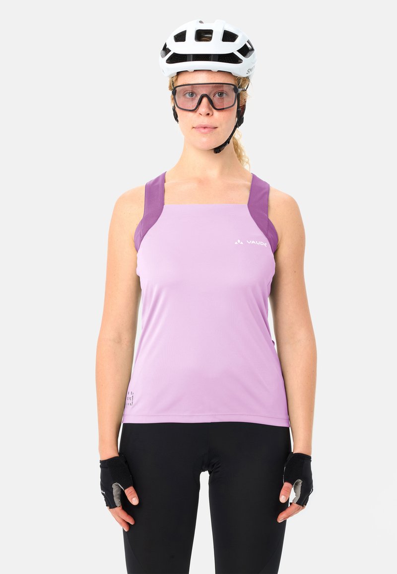 Femme portant un casque de vélo blanc, un haut de sport sans manches violet, des gants de cyclisme noirs, un legging noir et des lunettes de protection transparentes.