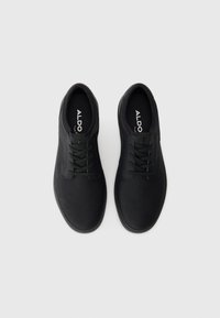 Zapatos negros con cordones, de textura suave similar al cuero y punta redonda. Presentan costuras sutiles y una plantilla acolchada con marca.