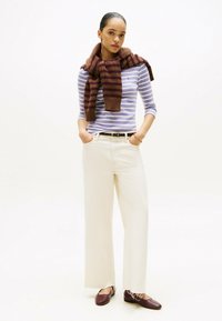 Gestreiftes, hell-lila langärmliges Oberteil, bequeme, beige weite Hose, brauner und burgunderfarbener gestreifter Schal, braune Ballerinas und ein schwarzer Gürtel.