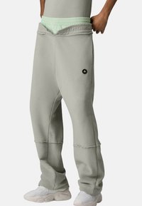 Lichtgrijze joggingbroek gemaakt van zachte stof, met een rekbare mintgroene tailleband en een vooraan logo, met een losse pasvorm en zichtbare stiknaden.