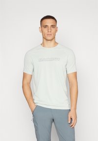 Lys grå t-skjorte med kort erm og "MAMMUT" logo i mørkere grå, laget av et glatt og pustende stoff. Har rund hals og raglanermer.