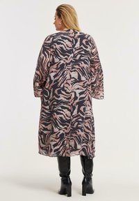 Langes, leichtes Kleid mit einem rosa und schwarzen Zebra-Muster, weit geschnittenen Ärmeln und geradem Schnitt, kombiniert mit knielangen schwarzen Stiefeln.