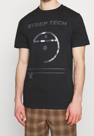 Mustat puuvillapaidat, joissa on metallinhohtoinen hopea "STEAP TECH" -teksti ja pyöreä grafiikkasuunnittelu edessä. Lyhyet hihat, pyöreä kaula-aukko.