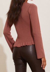 Maglione a maniche lunghe a costine in rosa polveroso con un corpo aderente e una gonna a balze svasata. Abbinato a pantaloni in pelle marrone scuro.