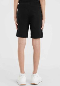 Svarta bomullsshorts med elastisk midja, knälånga och dubbelsydda fållar. I kombination med vita sportskor.