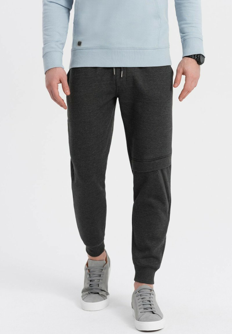 Donkergrijze joggerbroeken met elastische tailleband, trekkoord en zijzakken, gecombineerd met lichtgrijze sneakers en een lichtblauwe sweatshirt.