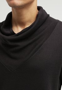 Svart, mjuk trikåtröja med en draperad halsdesign och en djup V-formad halsringning. Slät yta och sömlösa kanter.