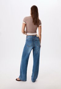 Wide-leg blue denim jeans with a faded finish, featuring two back pockets and a high rise. Paired with a brown fitted top.