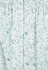 Tecido branco com estampado floral verde, apresentando várias flores pequenas e folhas, fecho de botão e detalhes plissados.
