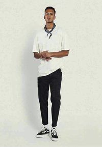 Λευκή oversized μπλούζα, μαύρο tapered παντελόνι, μαύρα και άσπρα παπούτσια και μια ψάθινη μαύρη μαντήλα γύρω από το λαιμό.