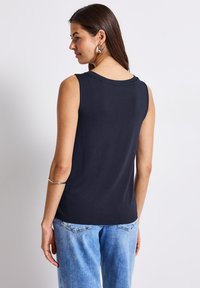 Marinblå ärmlös topp med rund halsringning. Tillverkad av mjukt tyg, har en baksidesdesign med subtila sömmar och en avslappnad passform.