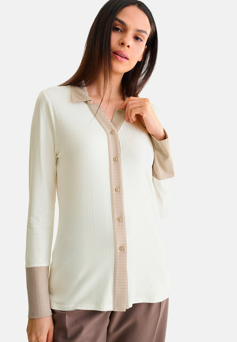 Knoop-up blouse in crème en beige, met ribbeltextuur, een contrasterende kraag en lange mouwen met kleur-geblokte manchetten.