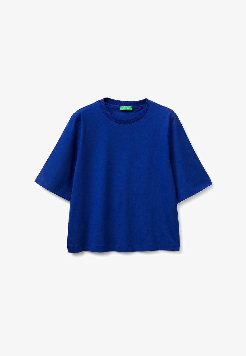 Camiseta azul de manga corta, de gran tamaño, con cuello redondo y etiqueta verde en el interior del cuello, mostrada sobre un fondo blanco.