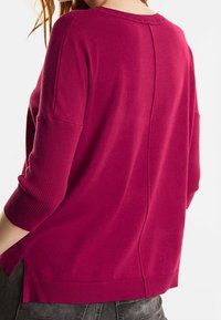 Fuchsiarosa pullovertröja med ribbat mönster, trekvartsärmar, sidsprund och rak baknaht. Mjuk stickad kvalitet.