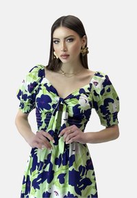 Vestido con estampado floral que presenta una paleta de colores en verde y azul marino, mangas abullonadas y un lazo en la parte delantera. Fabricado con una tela ligera y de textura suave.