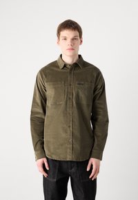 Olive green long-sleeve shirt in soft, textured fabric. Features button closure and two chest pockets. Simple, classic design.