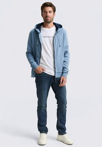 Svetlo modra jopa z zadrgo in žepi preko bele majice s kratkimi rokavi. Oblečena s temnimi kavbojkami in belimi supergami, prikazuje priložnostni videz.