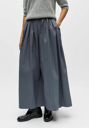 Grauer plissierter Rock aus leichtem Stoff, mit elastischem Bund in hoher Taille und seitlichen Taschen, kombiniert mit schwarzen Stiefeletten.