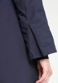 Marinskjortsärm med ett zippered öppning, som har ett mjukt syntetiskt tyg, förstärkt manschett och sydda detaljer längs sömmen.