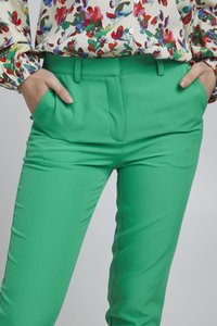 Groene op maat gemaakte broeken van soepel materiaal, met standaardzakken en voorplooien. Draag met een blouse met bloemenpatroon.