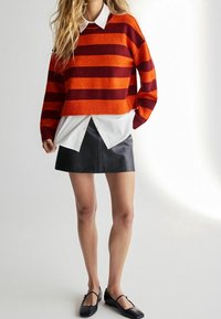 Gestreepte trui in rood en oranje, gelaagd over een witte blouse met kraag, gecombineerd met een zwarte leren minirok en zwarte ballerina's.