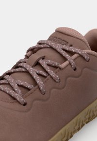 Chaussure de sport brune avec une tige texturée, ornée de lacets rose clair et d'un design ondulé. Semelle en caoutchouc avec un profilé pour une meilleure traction.