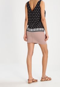 Top nero senza maniche con stampa geometrica bianca e bordo in pizzi, abbinato a una mini gonna fitted rosa chiaro. Modella indossa sandali marroni.