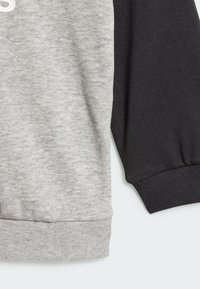 Top a maniche lunghe grigio e nero con texture a coste. Include maniche in contrasto e un polsino aderente all'orlo.