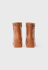 Bottines en cuir marron avec un bout arrondi, un petit talon carré, une fermeture à glissière sur le côté et une sangle décorative en métal doré.